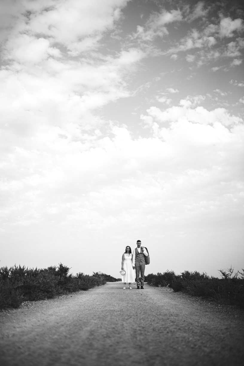 photo en noir et blanc, le couple de mariés marche sur un chemin, la perspective met les mariés en bas au milieu de la photo. 