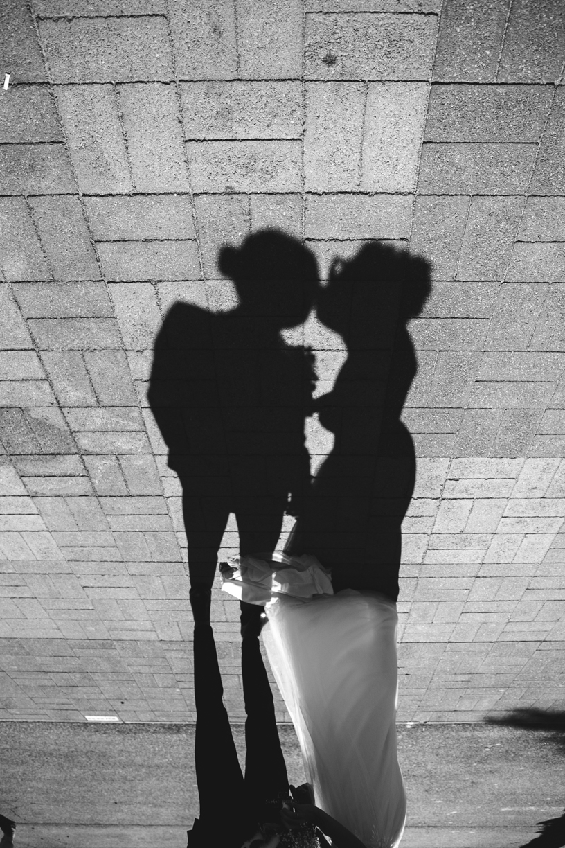 Photo de mariage en noir et blanc inversée, où l'on voit en silhouette par terre les mariés s'embrassaient